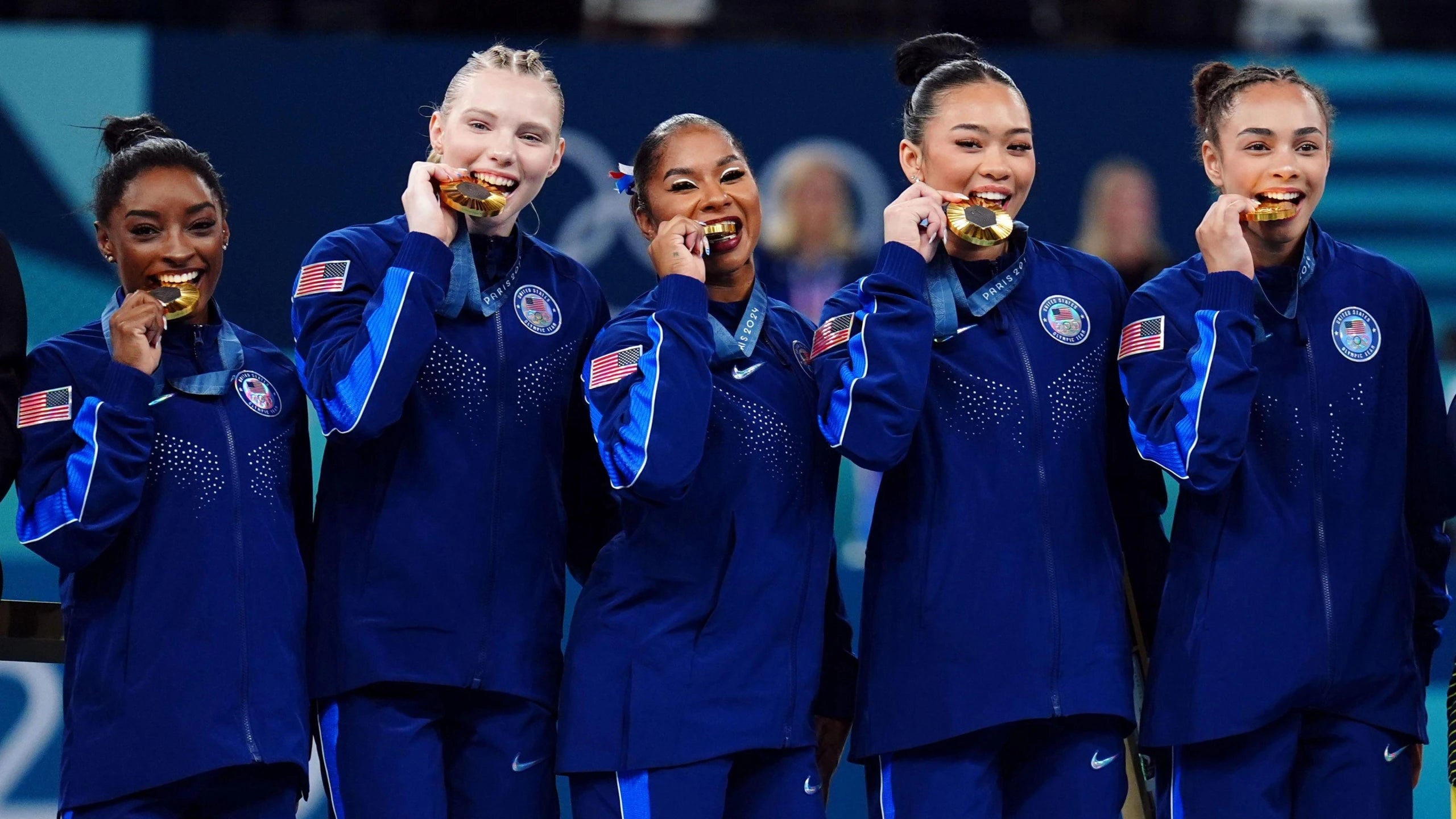Image of the American Gymnastics team biting their gold medals at the 2024 Paris Olympics